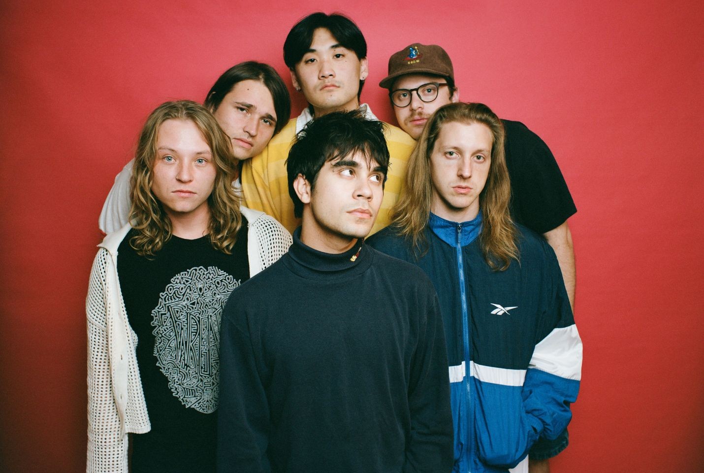 The six members of the band The Sophs in front of a red backdrop